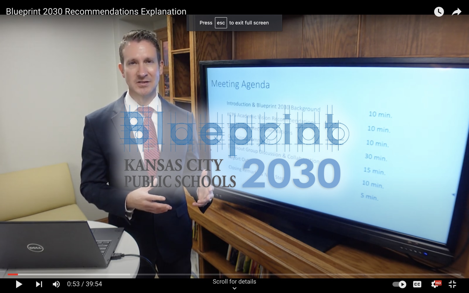 A man in a suit stands in front of a projector. The words Blueprint 2030 are on top of the video player.