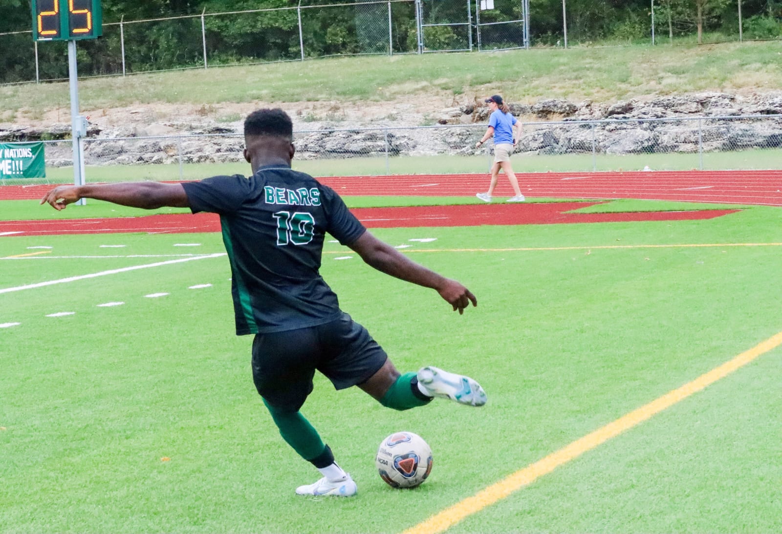 An East High School soccer player in black and green kicks a ball on the field.