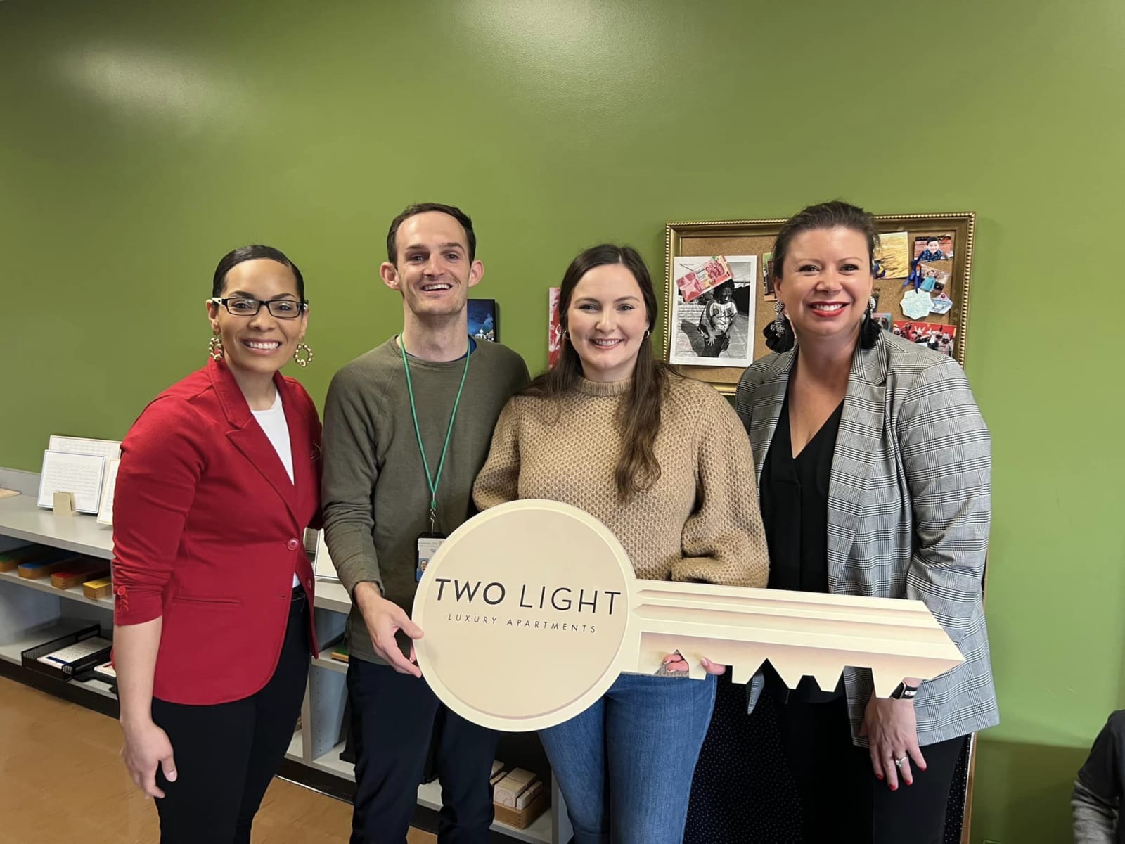 a group of smiling people holds a giant cardboard key in a green painted classroom