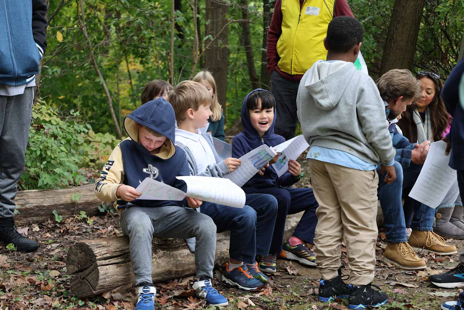Primary students reading together on a log in the woods