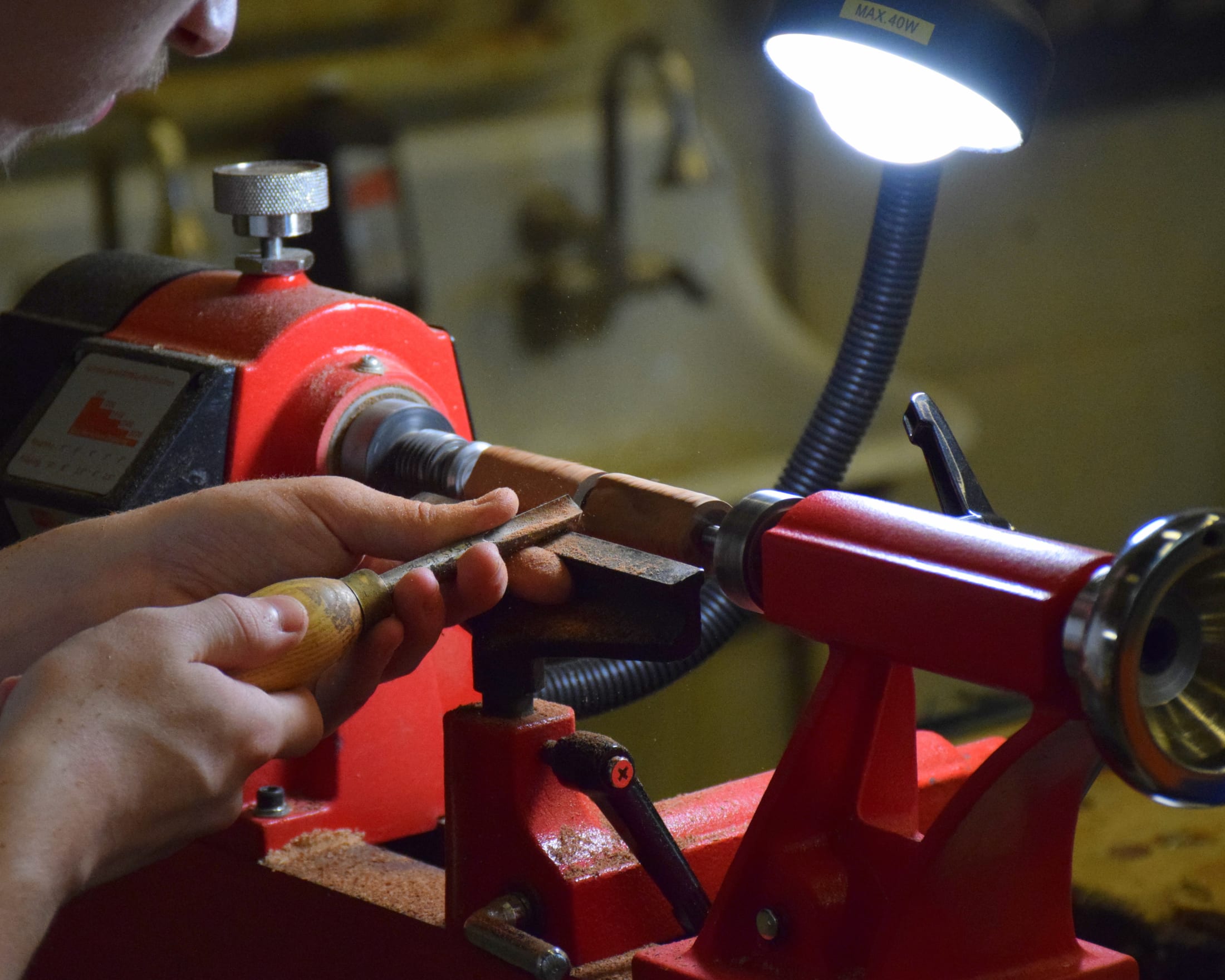 A person's hands are using a red power tool to work on a wooden object in a dimly lit workshop setting.