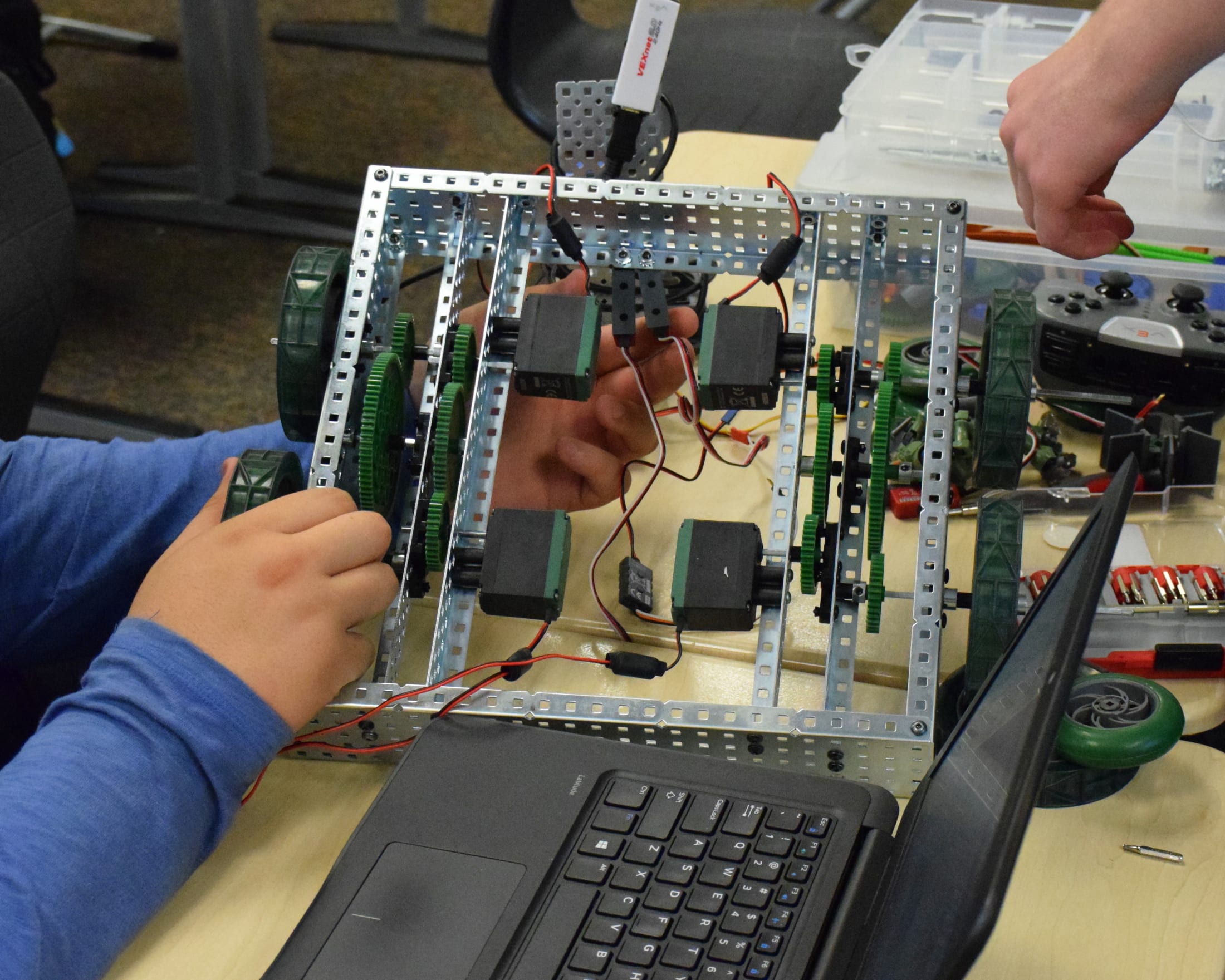 The image shows a person's hands working on an electronic device or circuit board, with various components and wires visible on a workbench or table.