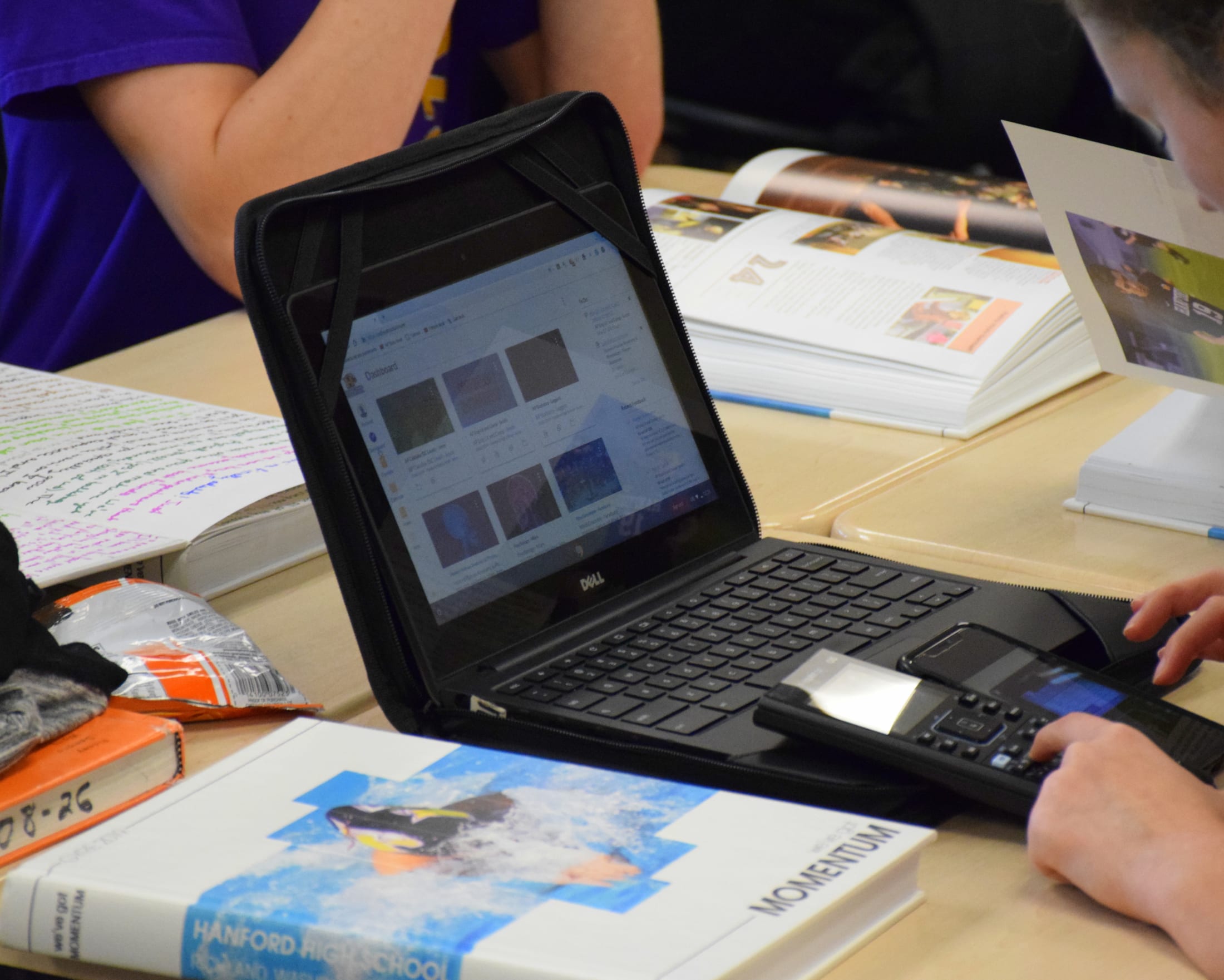 The image shows a person's hands working on a laptop computer, surrounded by various documents and materials on a desk.