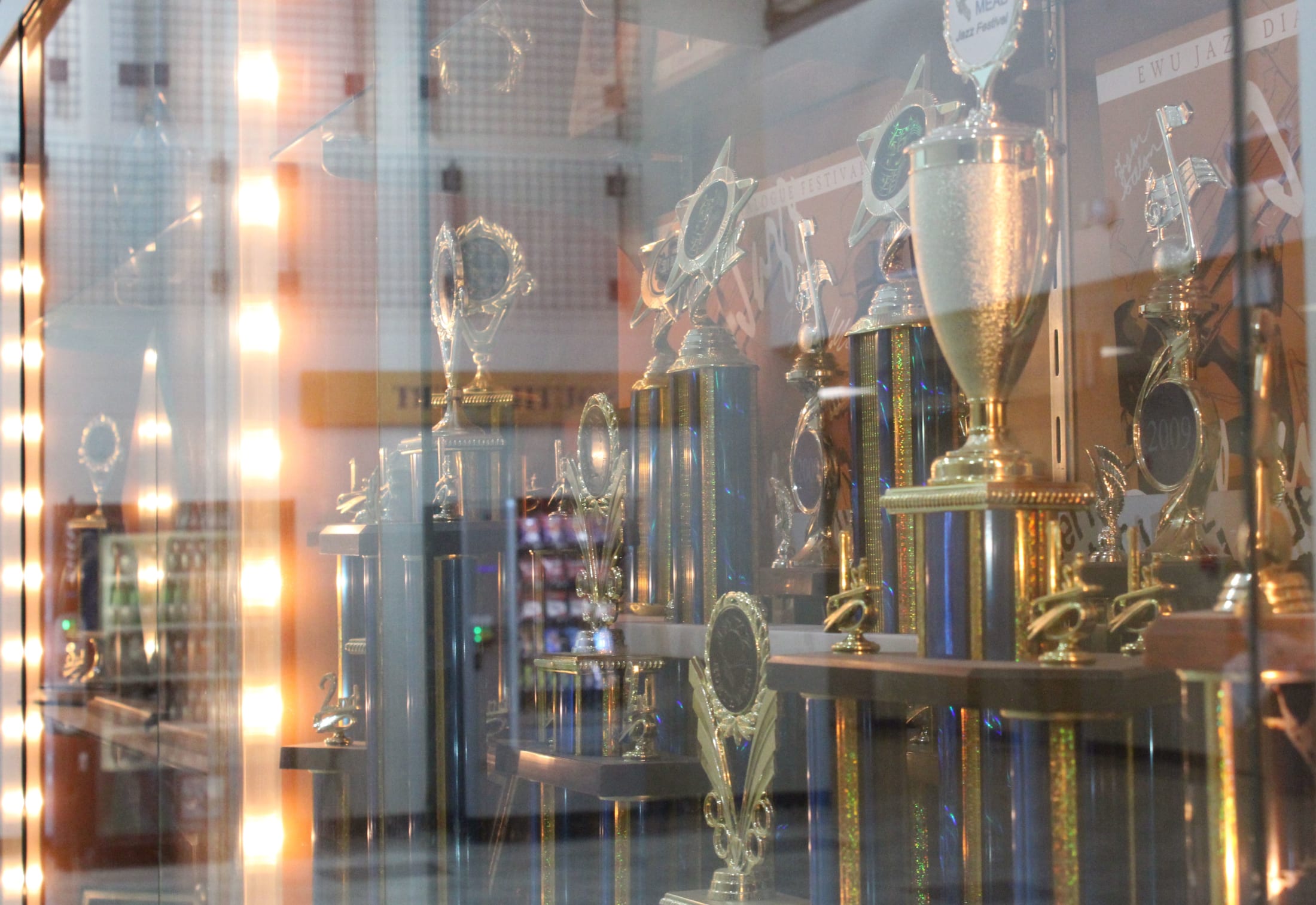 A display of various trophies and awards, some with gold and silver accents, can be seen through a glass enclosure, with the background appearing to be a dimly lit room.