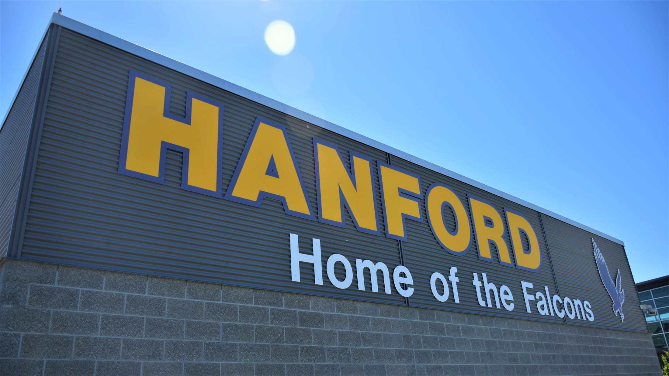 A large gray building with the text %22HANFORD Home of the Falcons%22 prominently displayed against a bright blue sky.
