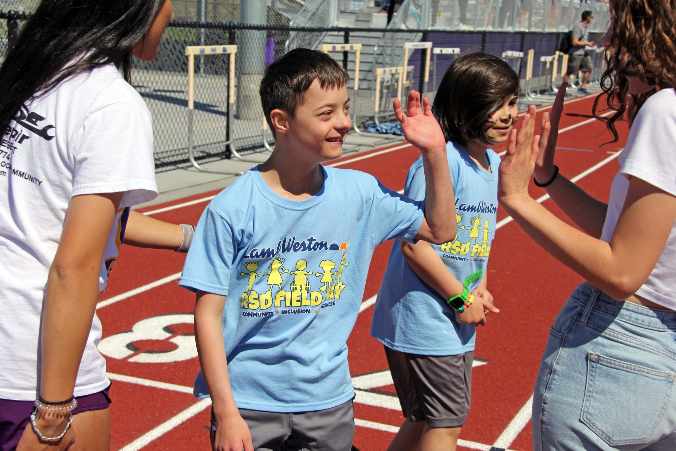A group of young people, likely students, are standing on a colorful running track, engaged in conversation and interaction with one another.