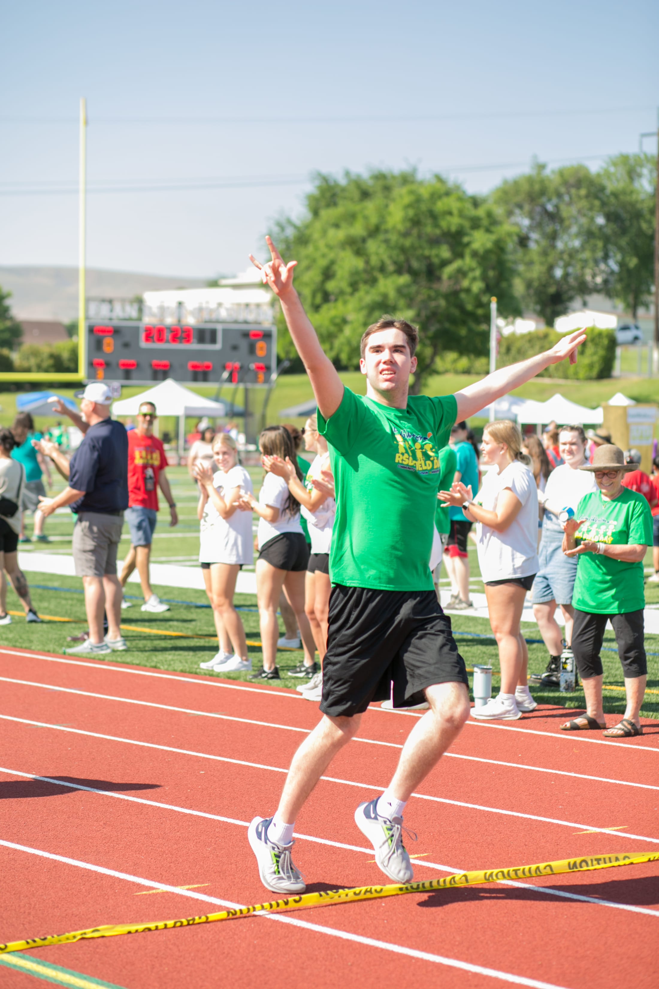 A man in a green shirt is running on a red track surrounded by a crowd of people in the background.