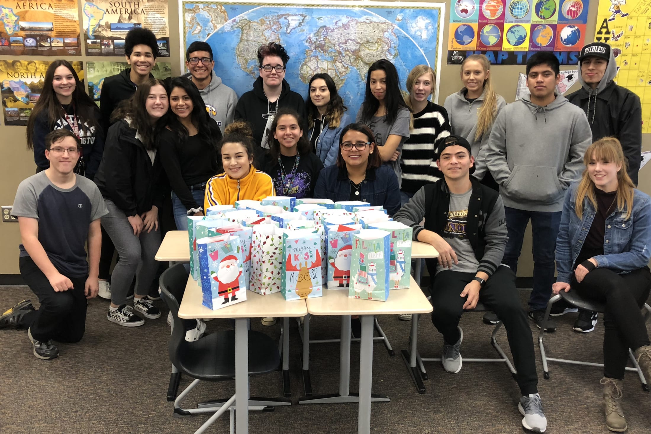 A group of young people, mostly students, are gathered around a table displaying various holiday-themed items and decorations.