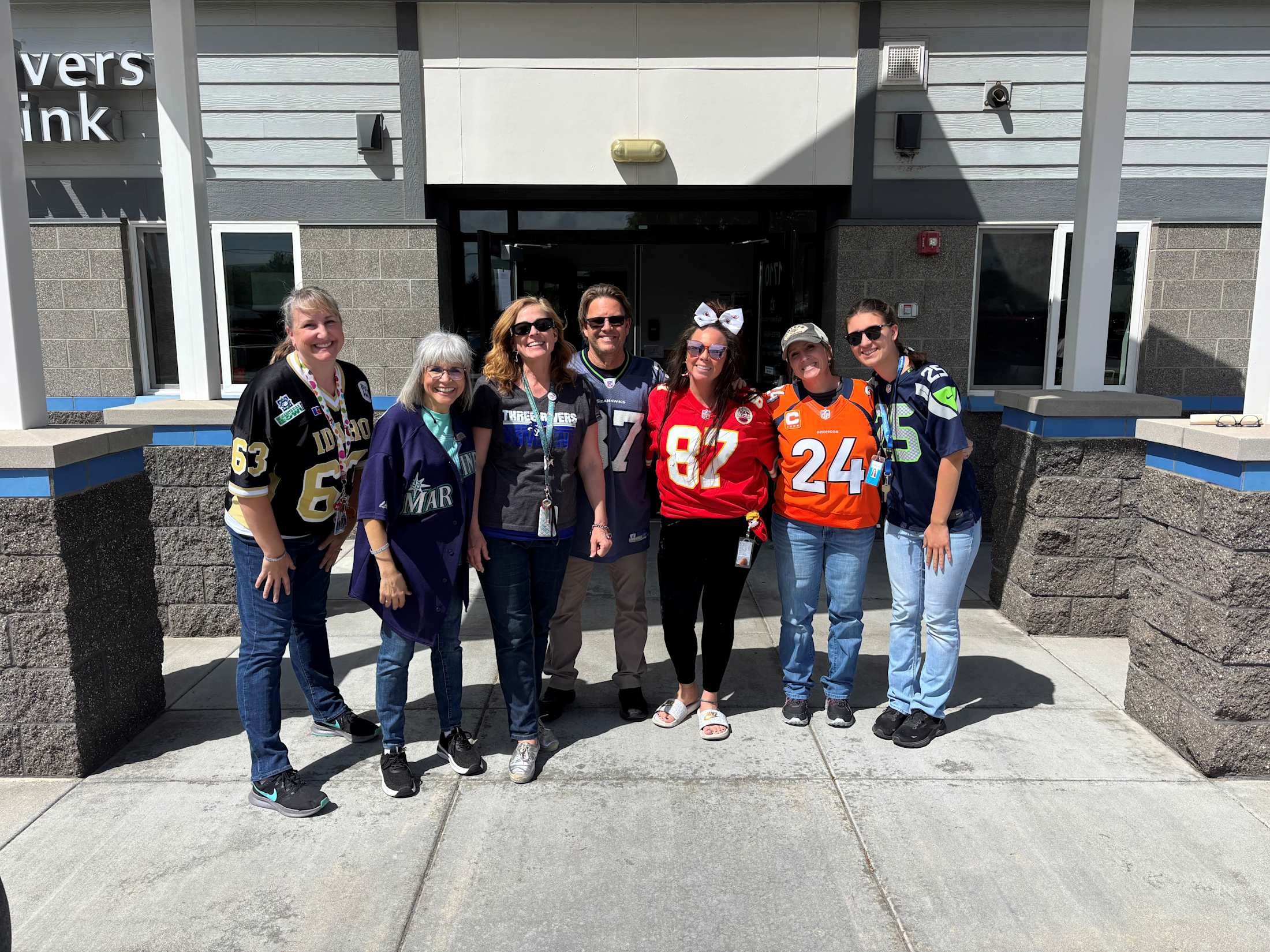 A group of people, some wearing sports jerseys, standing in front of a building with the name %22Vet's ink%22 visible.