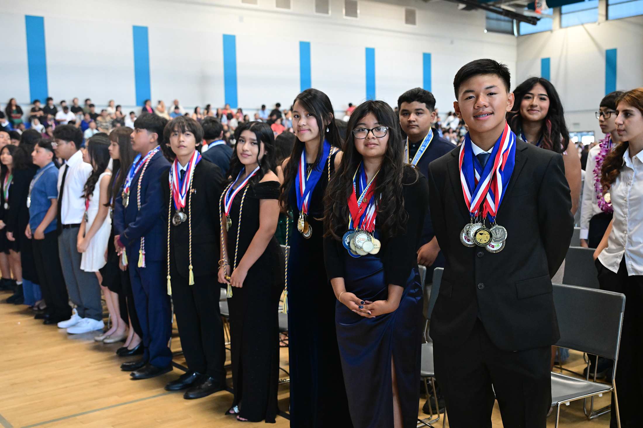 A group of students wearing medal while standing in a gym during graduation.