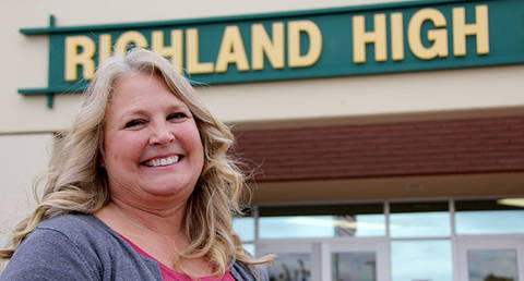 A smiling woman with long blonde hair stands in front of a sign that reads "Richland High".
