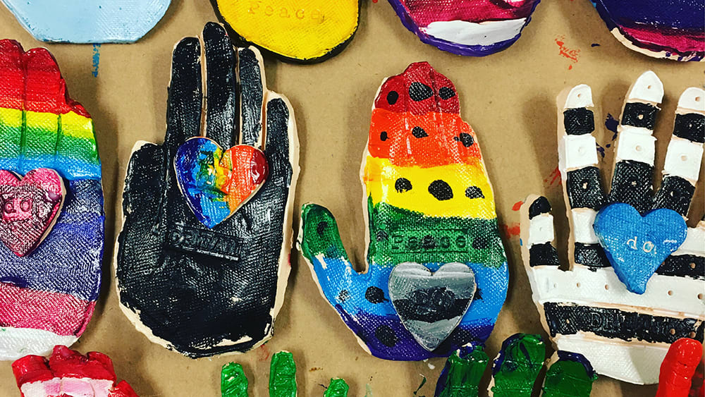 Colorful, hand-painted gloves and other artistic objects are displayed on a textured surface, creating a vibrant and visually engaging composition.