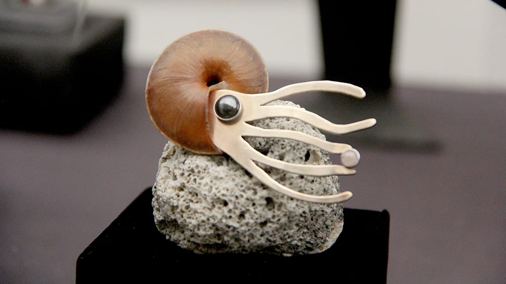 A small, white creature with large eyes and a distinctive shell-like structure appears to be perched on a dark, textured surface.