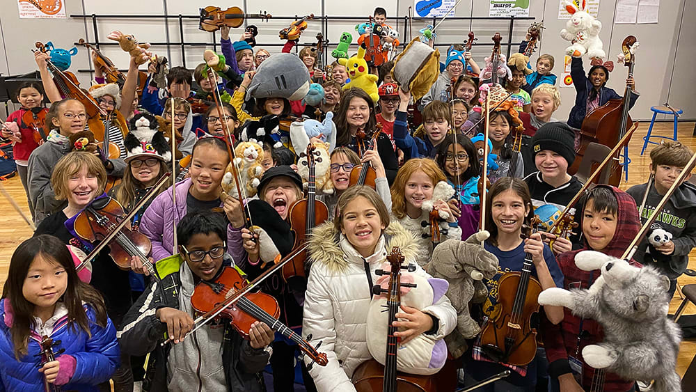 A large group of people, mostly young students, holding various musical instruments and posing together in a crowded room.
