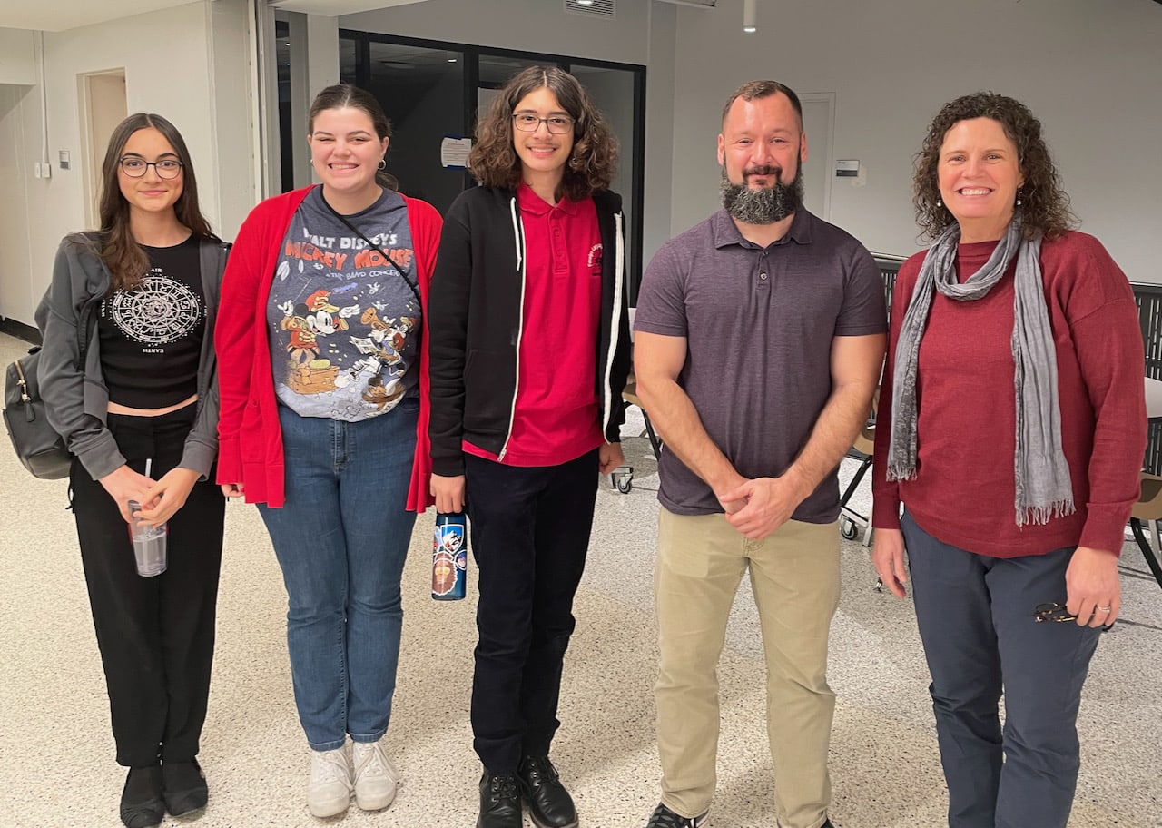 five people stand in a hallway smiling for a photo.