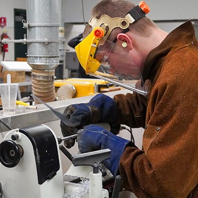A person wearing protective gear is operating a power tool on a piece of equipment in a workshop setting.