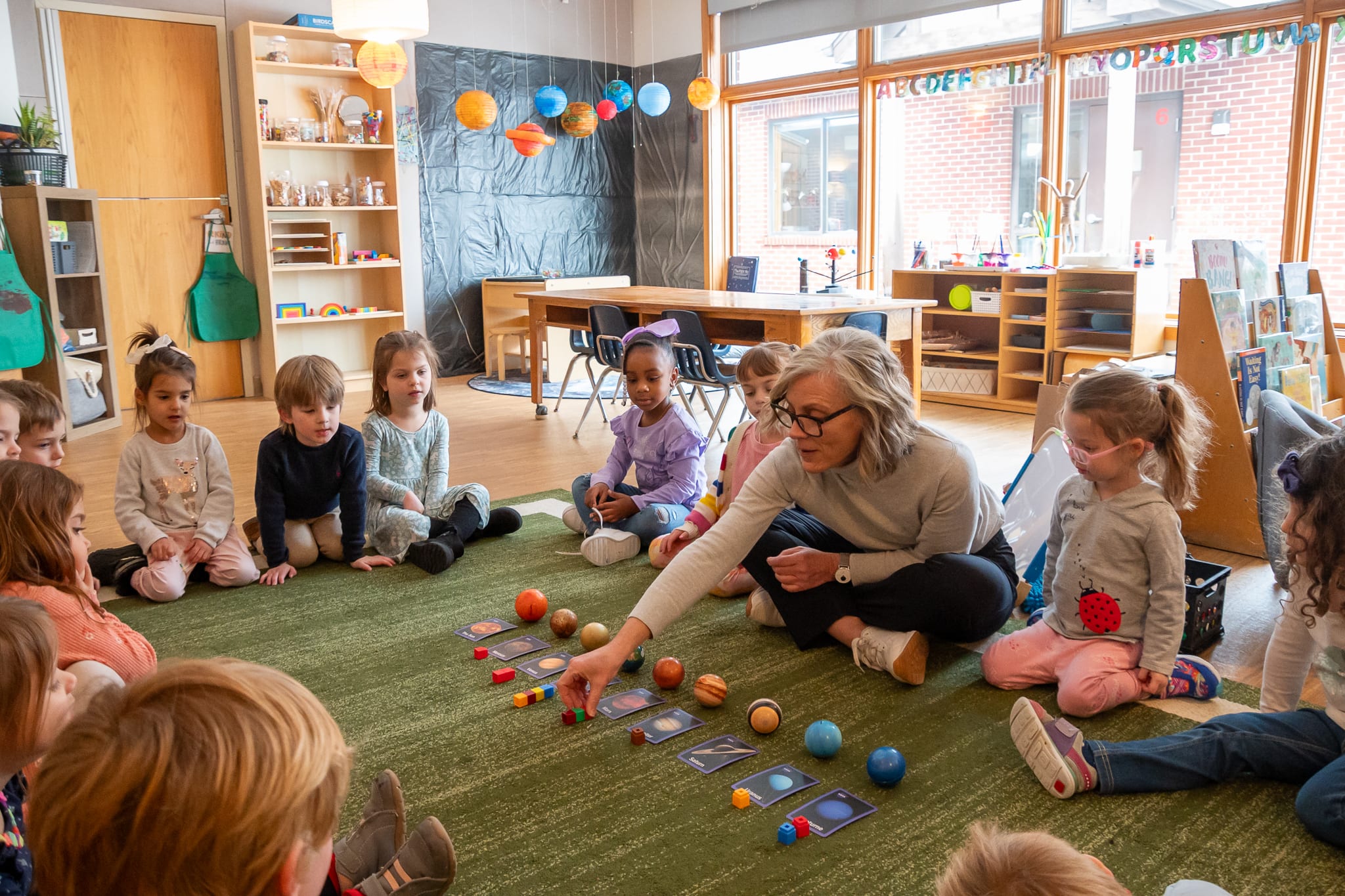 Preschool Teacher with students circled around a rug 