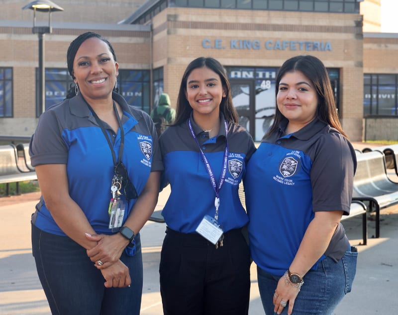 Three staff members from King Middle School standing outside on the first day of school in matching blue shirts with campus logos on them.