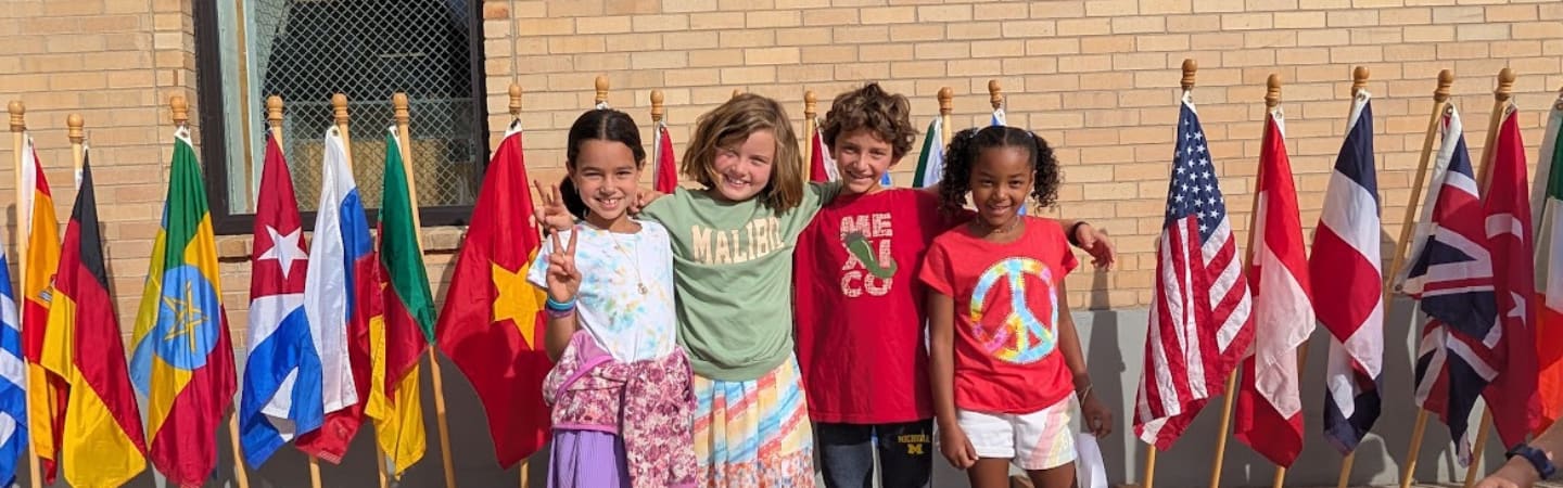 four students smiling and hugging in from of different flags 
