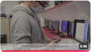 A man in a mask and gloves is focused on working at a computer, emphasizing safety and health precautions.