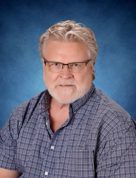 Man in 50s with gray hair and beard wearing glasses and blue checked shirt, professional headshot