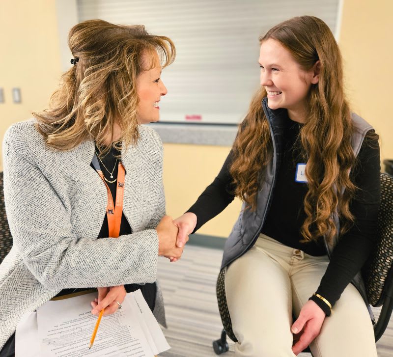 Professional handshake between a woman and a student during a networking event.