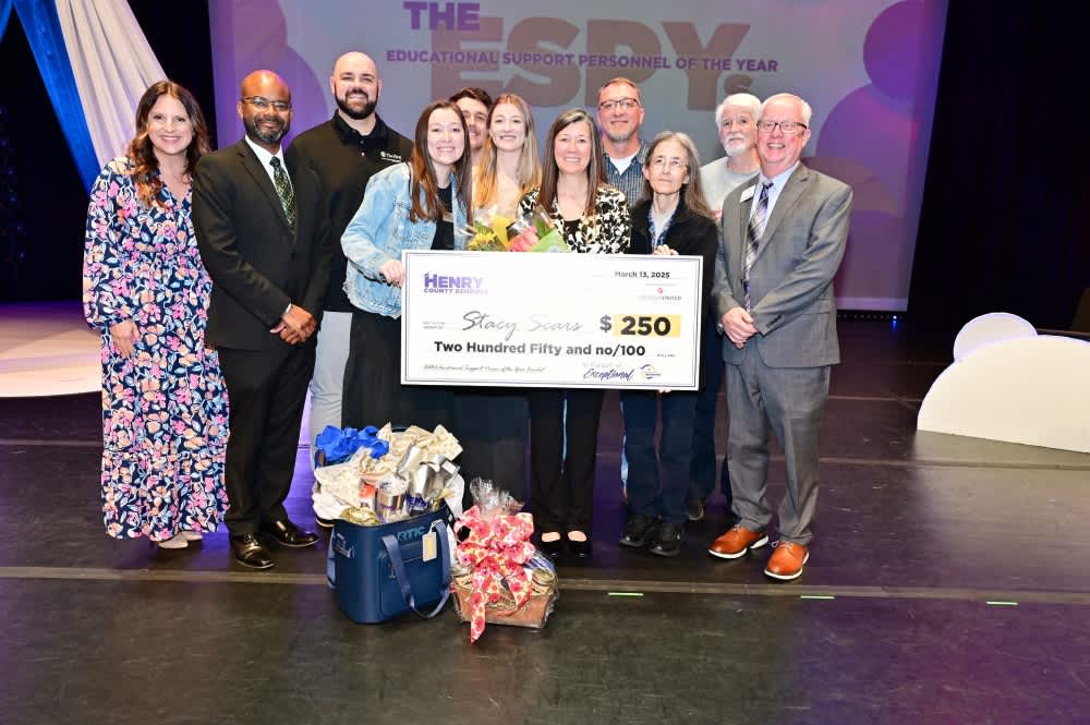 Sears on stage holding large check surrounded by family, Dr. Pace, and Steve Overcash