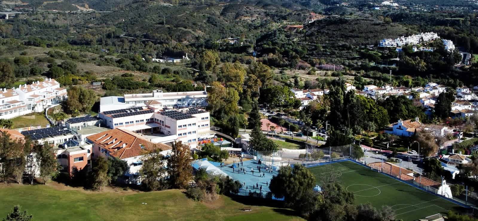 Aerial view of a large international school campus with sports courts and surrounding hills in Marbella