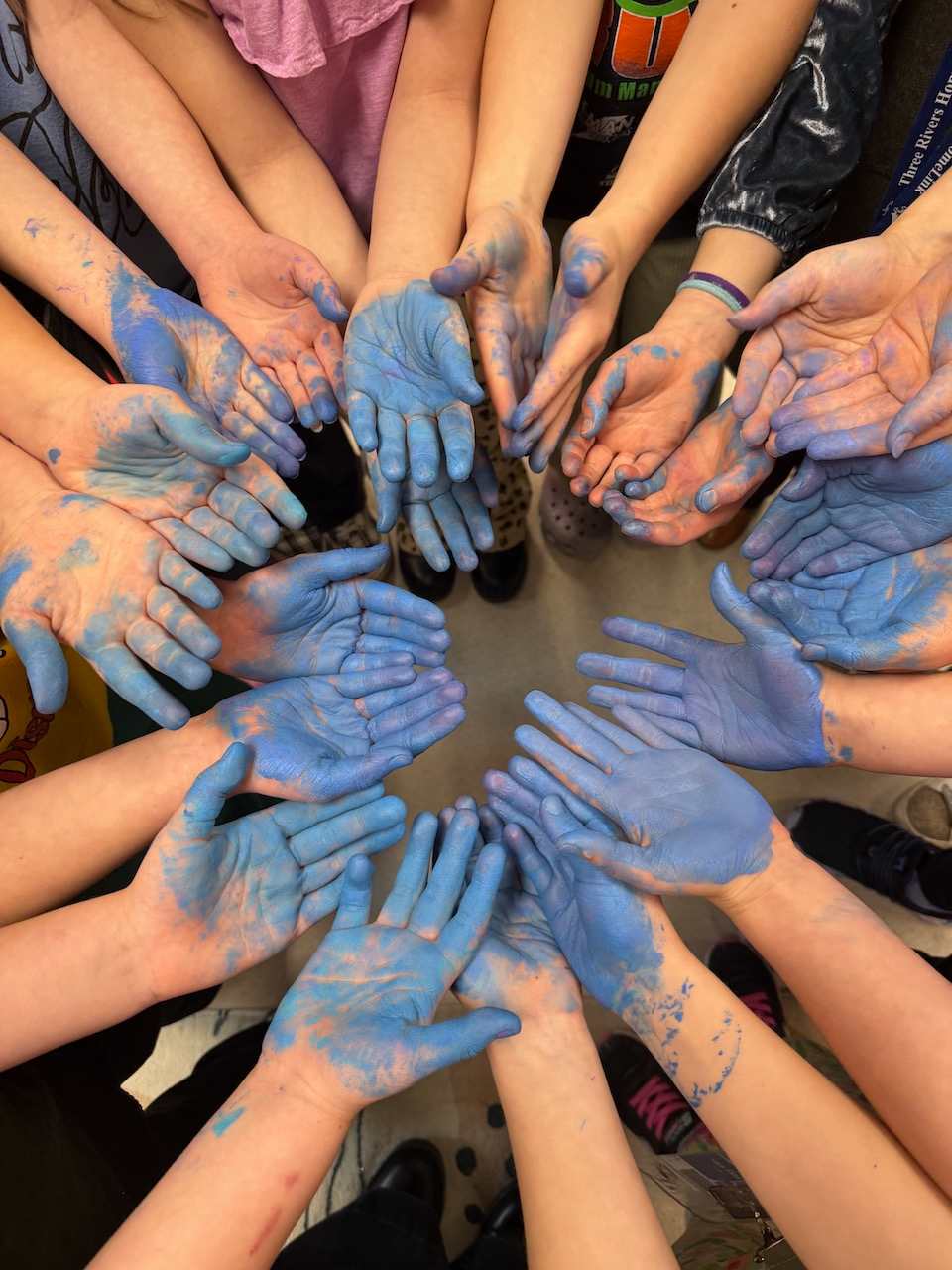 A group of hands, painted in various shades of blue, are arranged in a circular pattern, creating a visually striking and collaborative composition.