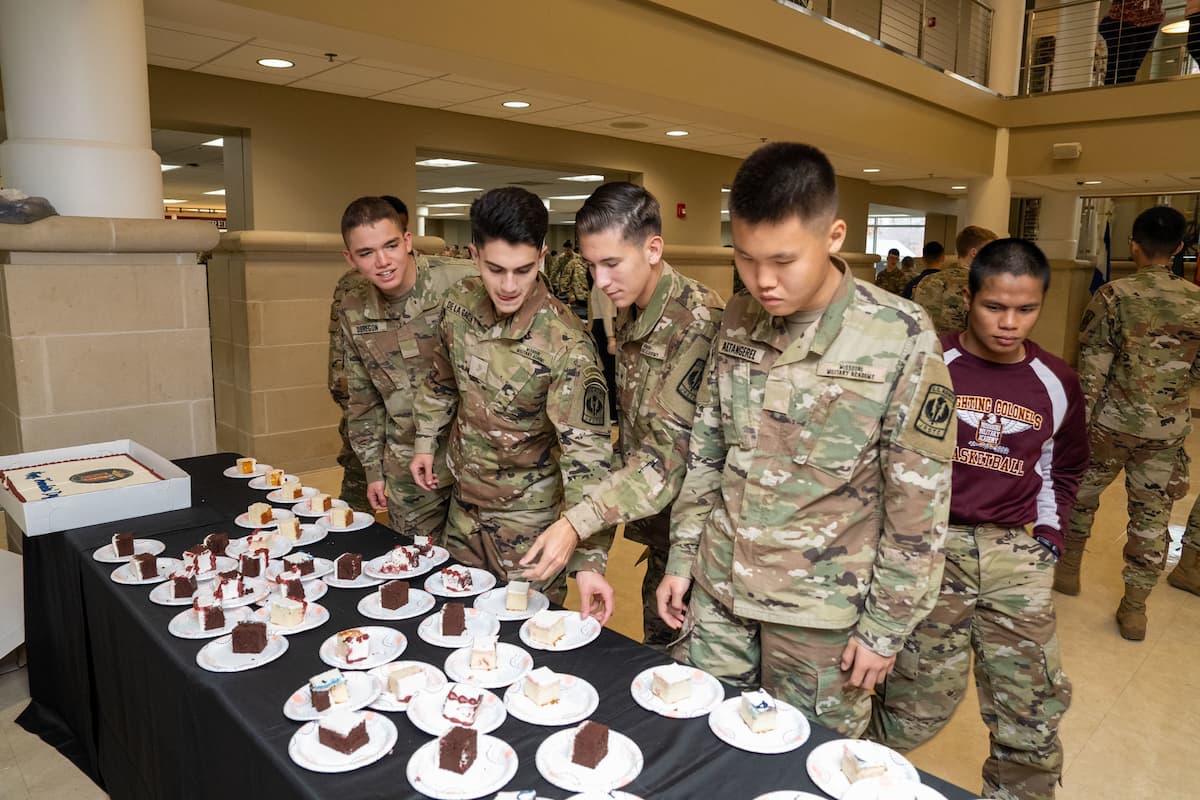 A group of military academy middle and high school cadets gather around a table to get cake.