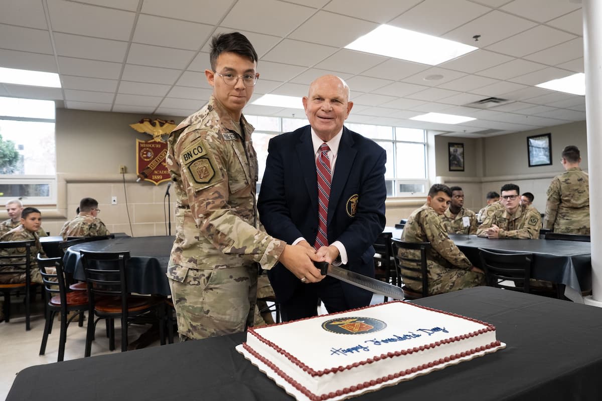 MMA cadet battalion commander and President Richard V. Geraci stand behind a cake on a table in front of them.