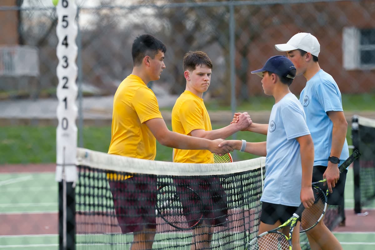 Four tennis players shake hands across the tennis net.