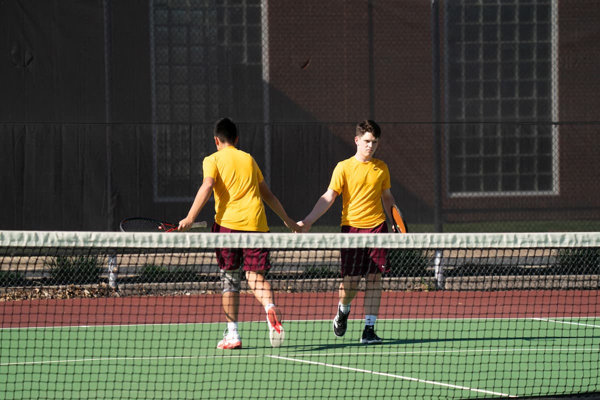 Cadets Scribner and Reyes high-five on the tennis court during a match.