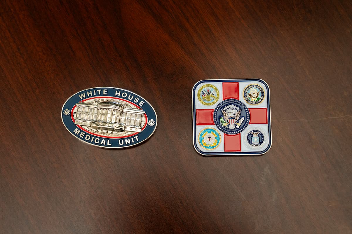 White House Medical Unit and military service challenge coins displayed on a wooden table.
