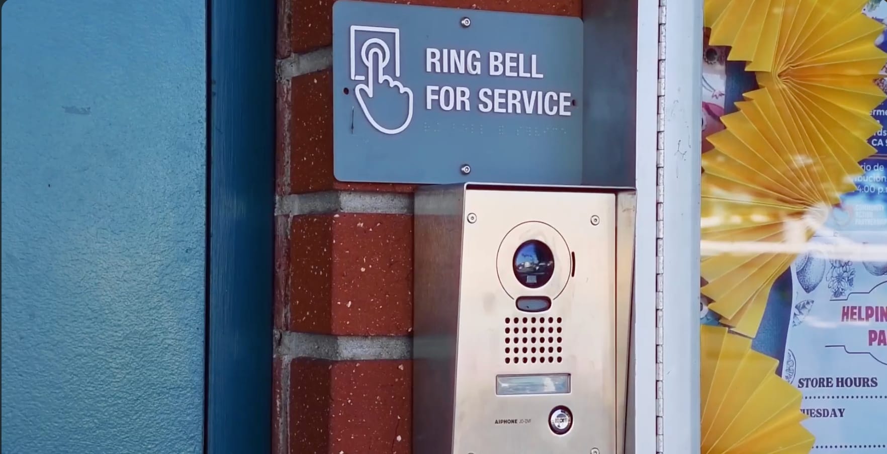 A brick wall with a stainless steel camera with a sign that reads ring bell for service.