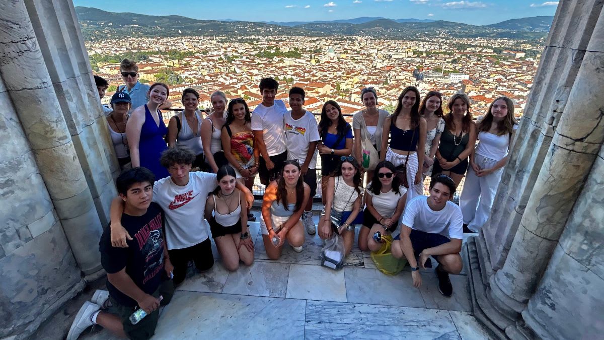 A group of young people poses for a photo on a marble platform with a sprawling cityscape in the background.