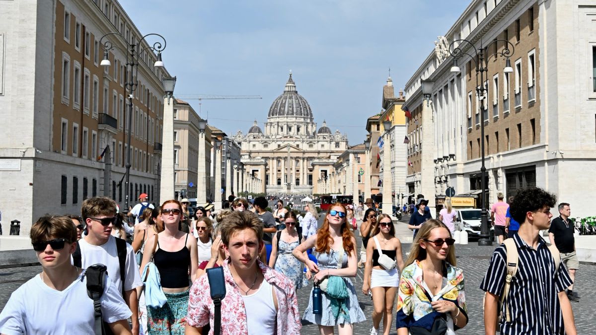 A crowd of tourists walks down a wide street towards St. Peter's Basilica in Rome.