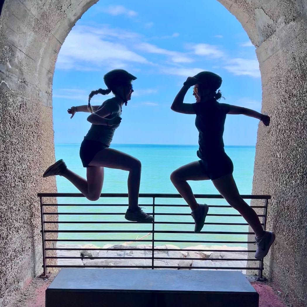 Two CCI students jumping beneath a stone arch overlooking the Adriatic