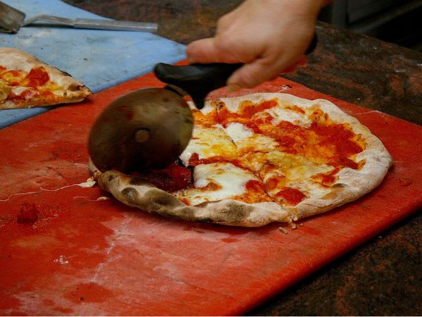 A freshly prepared pizza is sliced in the kitchen