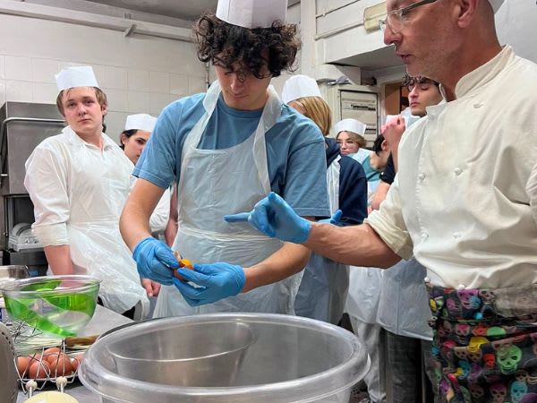 A student measures an ingredient in a professional kitchen