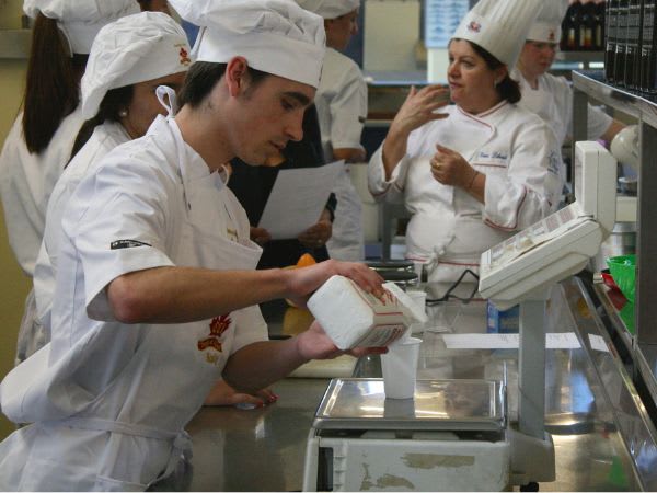 A student practises a cooking technique under a chef's guidance