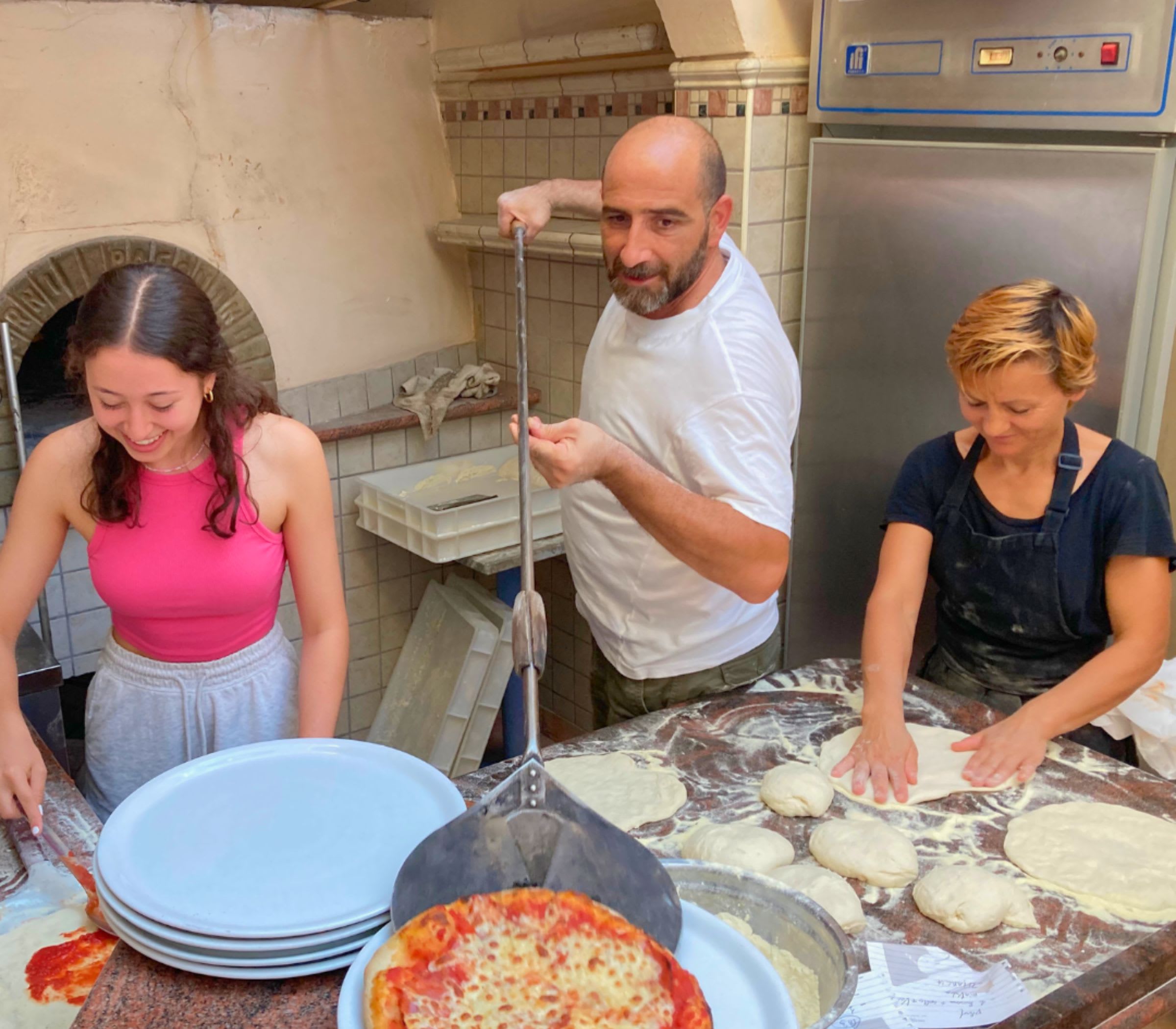 A CCI student learning to prepare pizza beside Allegria's wood-fired oven