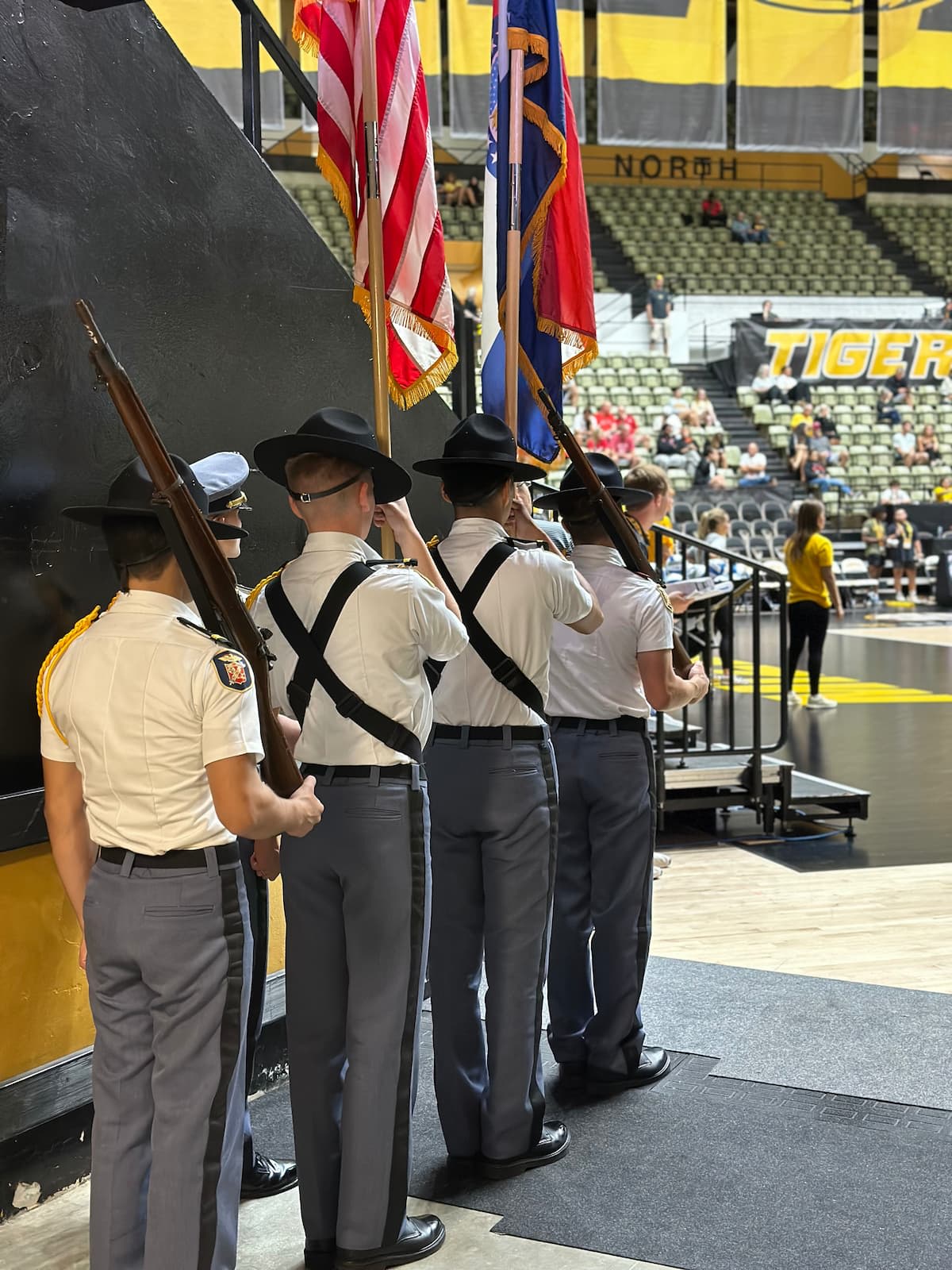 MMA cadets in uniform stand in formation with flags inside a stadium