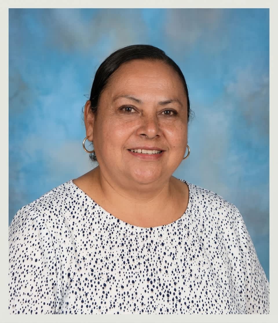 A woman wearing a black and white patterned shirt and hoop earrings smiles against a mottled blue background.