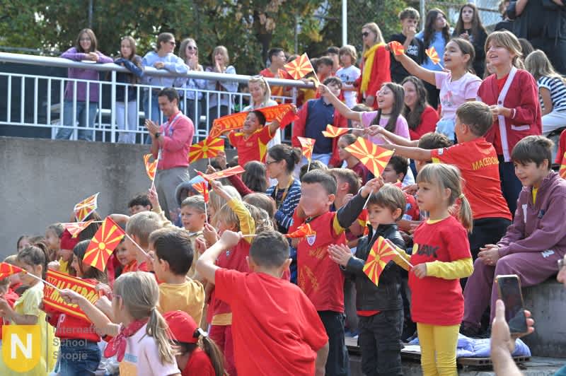Students waving red and yellow North Macedonian flags at the Parade of Nations