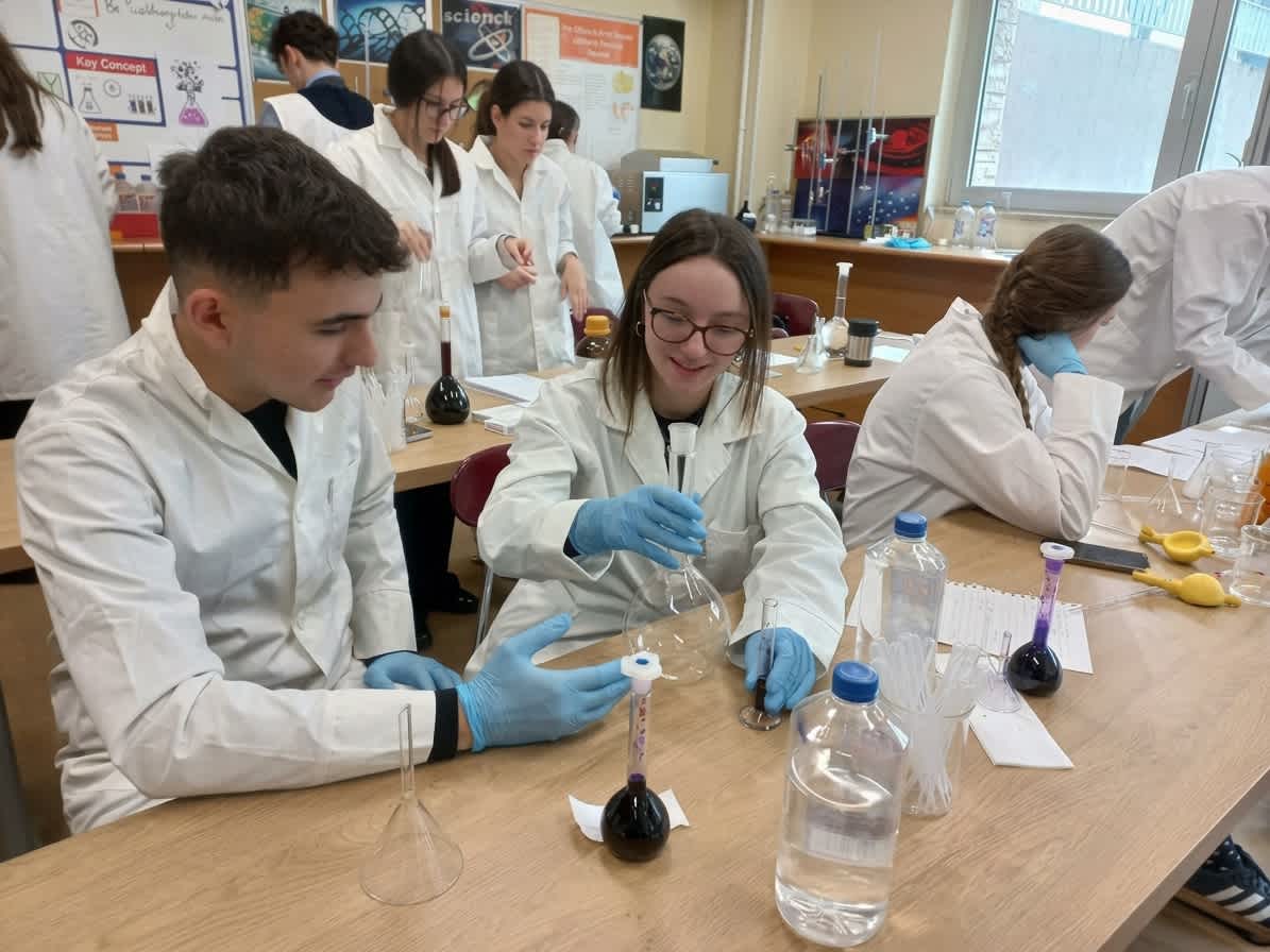 Secondary students in lab coats measuring solutions during a chemistry experiment
