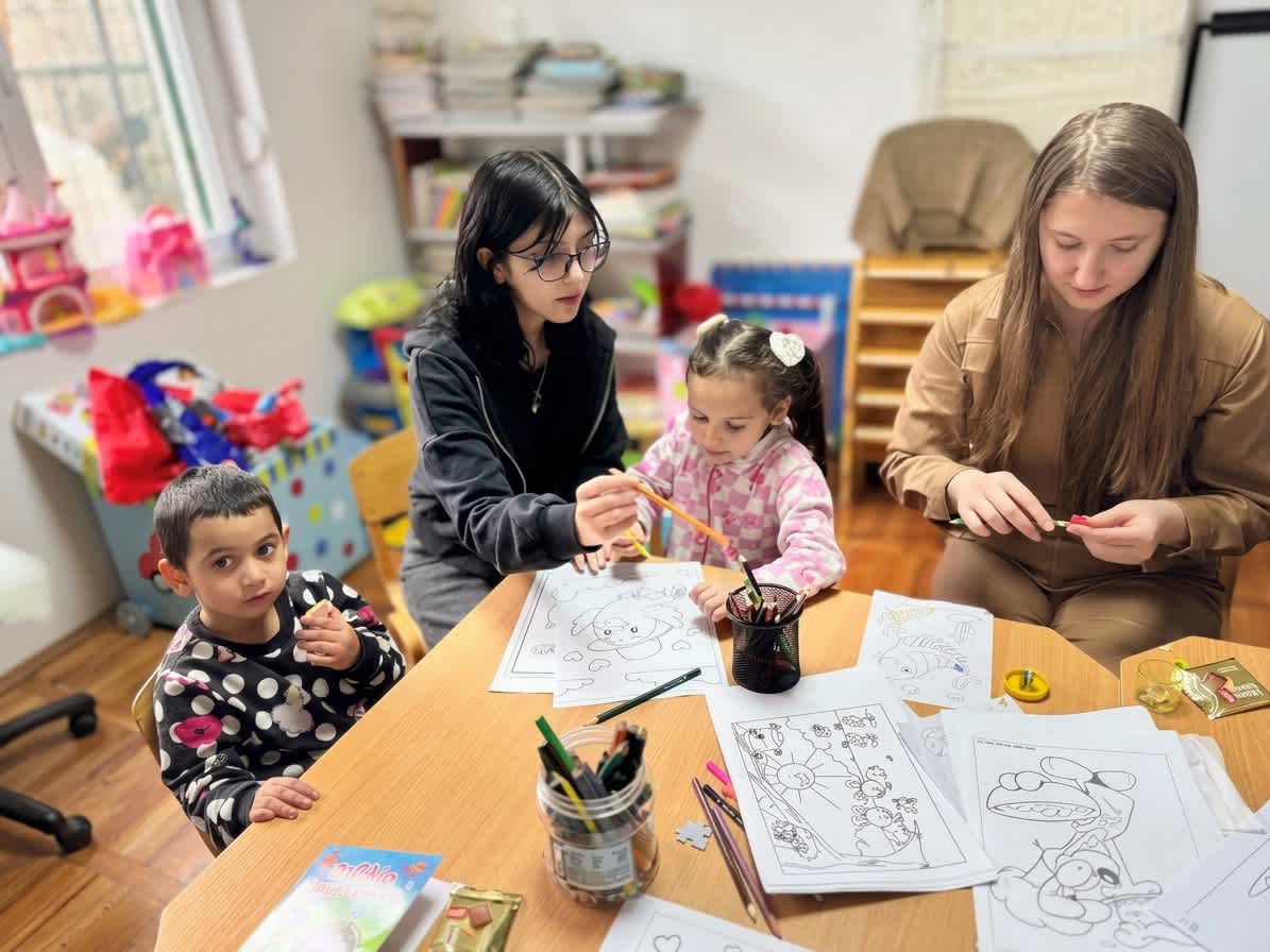 Older students sitting with young children, helping them color pictures