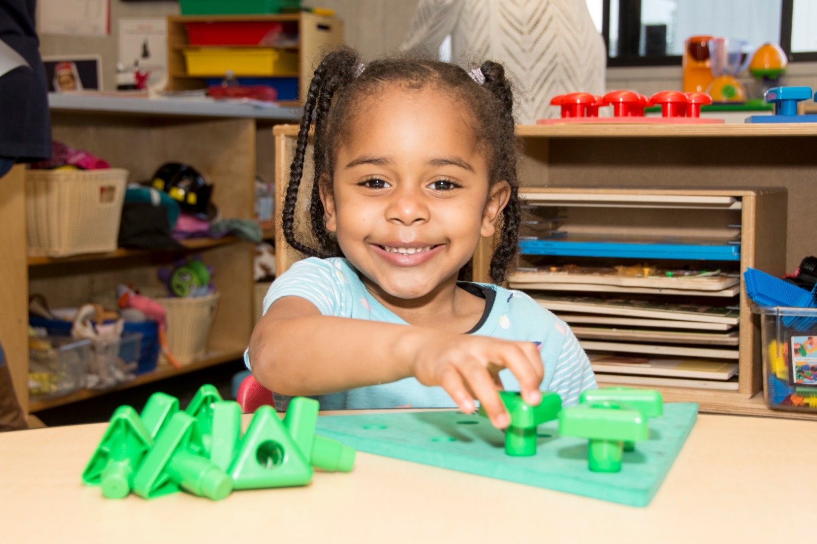 A young girl with braided hair is sitting at a table, playing with colorful building blocks.