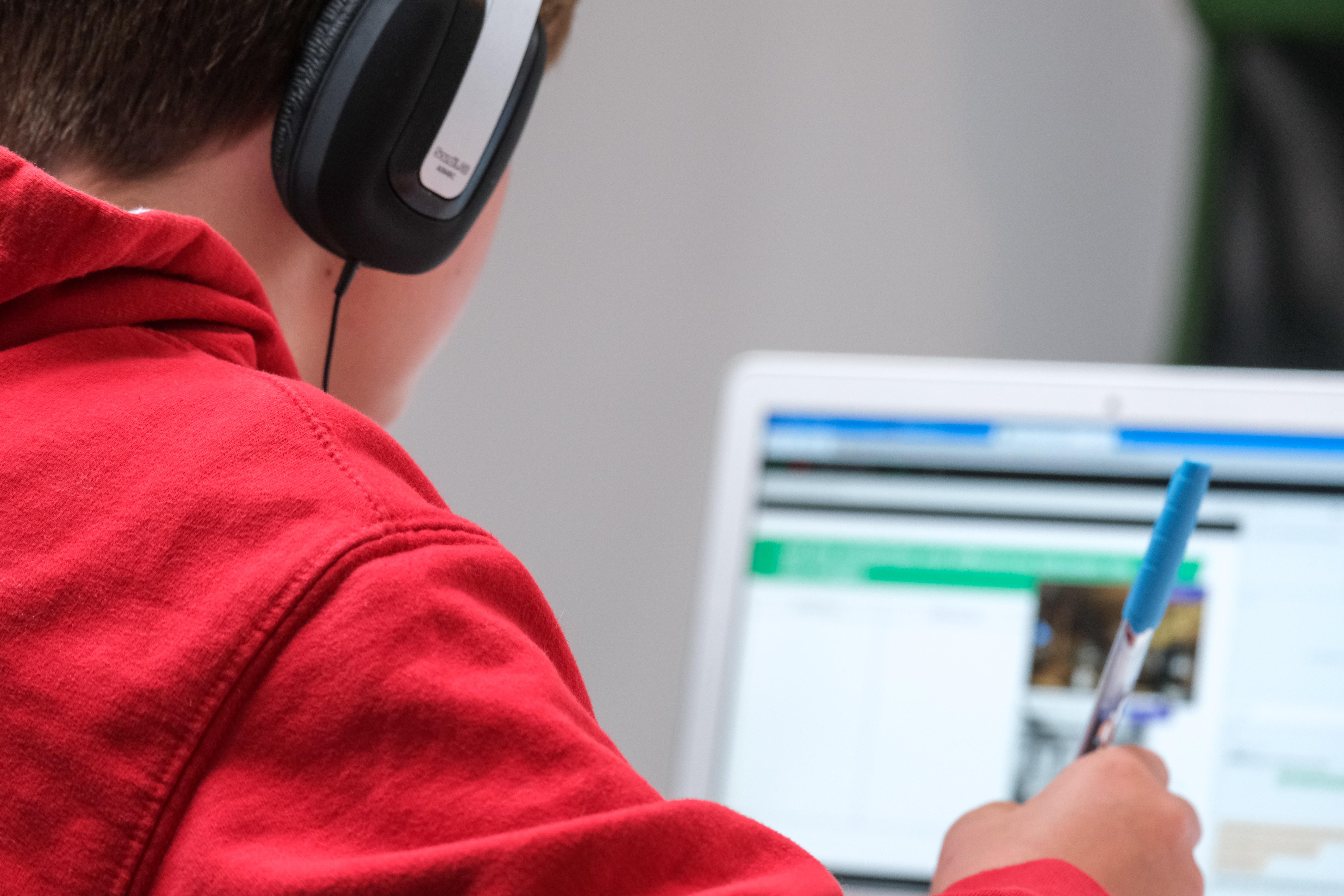 Boy with headphones taking notes in front of computer