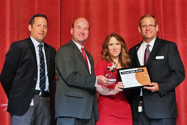 Four people stand in front of a red curtain, with two men on the left and two people on the right, one of whom is receiving an award.